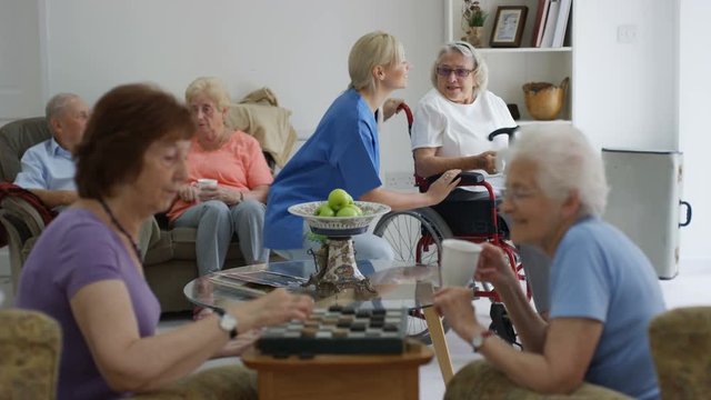 Young caring nurse talking to and taking care of residents in retirement home.