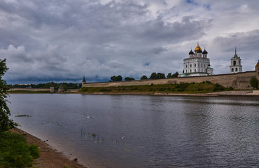 Fototapeta na wymiar Kremlin of Pskov. The view from the river Great/Summer, evening. The sky is covered with clouds. A gull flies over the river. On the opposite bank is the Pskov Kremlin. Russia, Pskov region, landscape