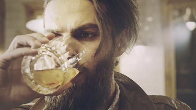 Handsome bearded man drinking brandy. Close up of beard man drinking whiskey. Manly man drink glass. Bearded hipster face. Male beard portrait. Drinking man face