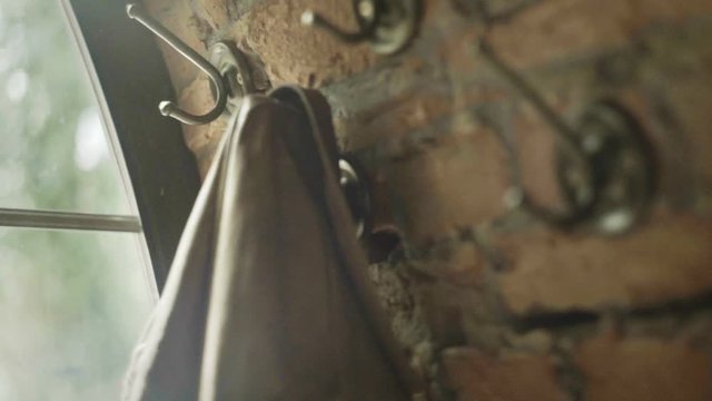 Vintage clothes hook on brick wall. Retro wardrobe near the window. Male hand putting jacket on wall hanger vintage style. Wall clothes hanger. Man hands put clothes hanger