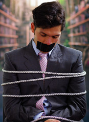 Businessman trapped in a chair with rope, with a black tape in his mouth in a blurred background