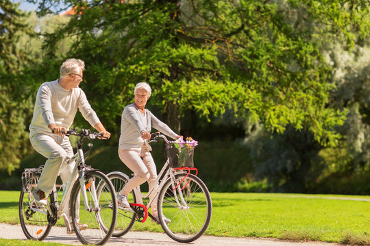 happy senior couple riding bicycles at summer park