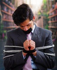 Businessman trapped in a chair with rope, with a black tape in his mouth and hands in a blurred...