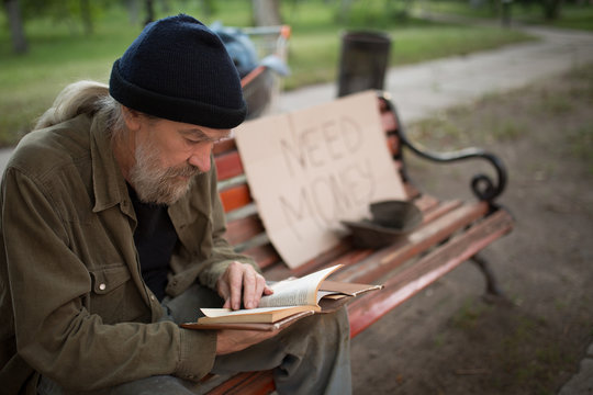 Close up view of old man reading while sitting on bench. Homeless man outdoors holding old book.