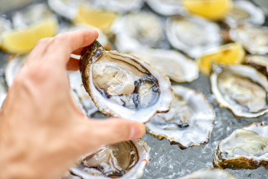 Open oyster in a male hand, against the background of open oyste