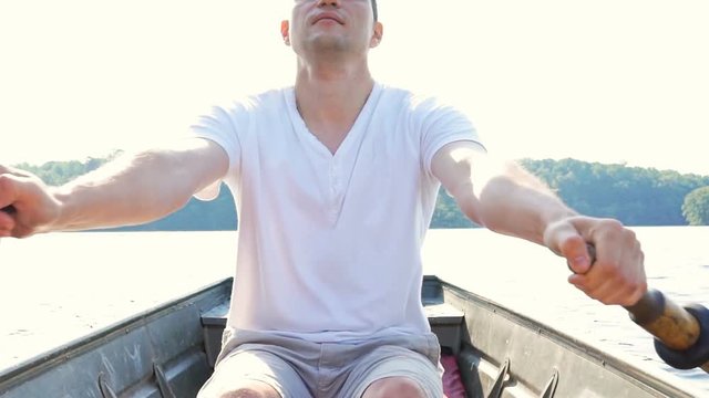 Serious focused concentrated young fit man rowing boat on lake in Virginia during summer in white shirt