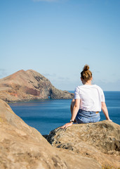 Fototapeta na wymiar Junge Frau sitzt auf einem Felsen und blickt in Richtung Meer