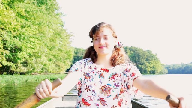 Happy young woman rowing boat on lake in Virginia during summer with warm, soft sunlight, sunshine, sun