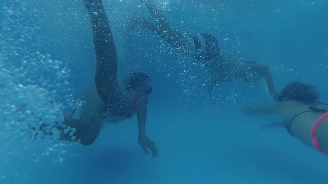 teen boy and girls swim under the water in the pool, back view, bubbles, sun rays