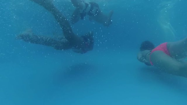 teen boy and girls swim under the water in the pool, back view, bubbles, sun rays