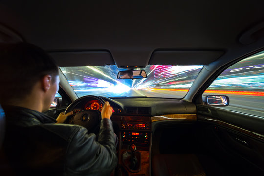 Driver in a car moves at fast speed at the autum night. Blured road with lights with car on high speed. Long exposure shot.
