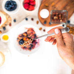 Top view showing hands eating porridge with honey nuts, blueberries on white wooden table selective focus, blurred background Good morning - healthy breakfast background