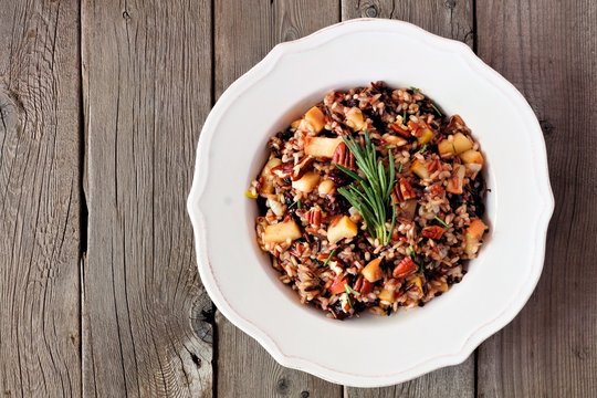 Autumn rice pilaf with apples and cranberries in a vintage bowl against a rustic wood background