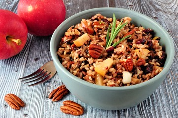 Autumn rice pilaf with apples, nuts and cranberries in a gray bowl against an old wood background