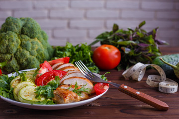 Diet concept, healthy lifestyle, low calorie food. Baked chicken breasts with zucchini and salad, measuring tape and vegetables on the table