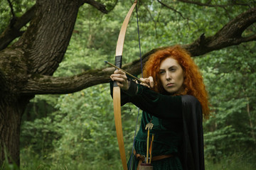 Fototapeta na wymiar Red haired girl shoots from the bow