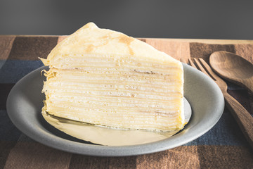 Crepe cake or milk cake in a plate with wooden spoon and fork on table cloth
