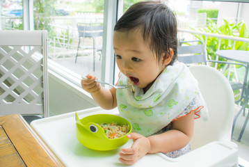 A child is eating with spoon by herself. Baby eating.