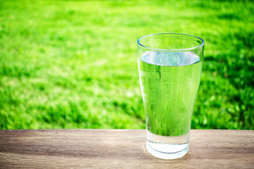 A glass of water on the table with green grass background.