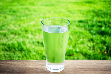 A glass of water on the table with green grass background.