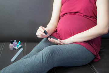 Pregnant woman painting her nails on sofa.