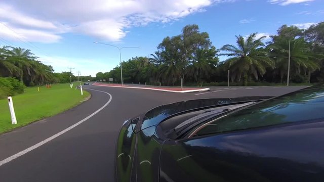 A gopro shot that is mounted on a black car. The car takes a highway that is surrounded by tall trees.