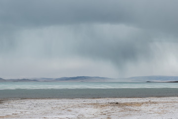 panoramic view of lake with snow on coast and storm clouds in sky

