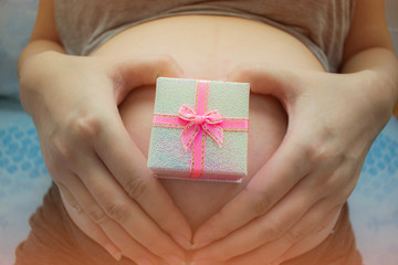 Pregnancy. Pregnant woman holding small present box on her belly.
