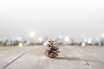 Pine cone sitting on rustic wooden surface with holiday lights and tinsel in soft focus