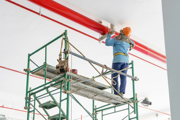 Worker painting the steel red pipe using a roller on the scaffold.