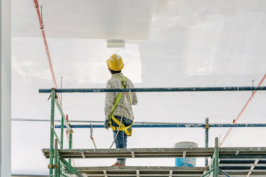 Worker man painting a gypsum plaster ceiling with paint roller on the scaffold