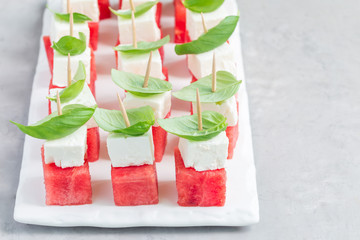 Watermelon salad or caprese with watermelon, feta and basil on white board, horizontal, copy space