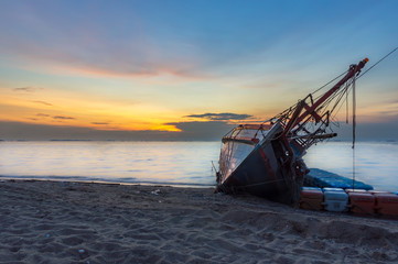  An old shipwreck or abandoned shipwreck, Boat capsized on the sand beach in beautiful colorful twilight sunset background with plastic tank movement