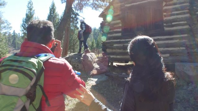 Dad taking photos of family by a log cabin in a forest, shot on R3D