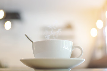 White cup with steaming hot coffee on table with bokeh background at cafe.