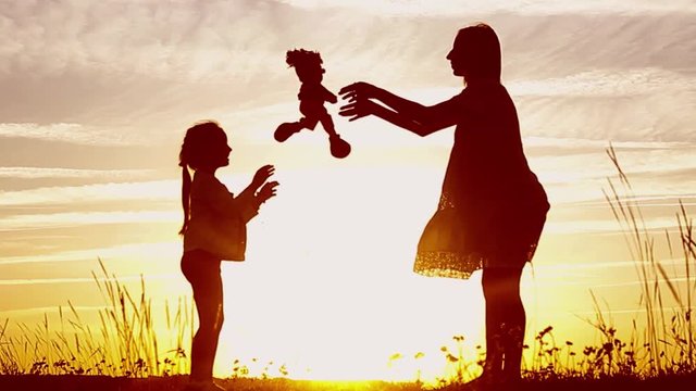 Silhouette of mom and daughter at sunset, holding toy doll and staring into the distance. Silhouette of girl play with dolls