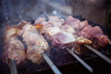 Grilled kebab cooking on metal skewers (grill). Roasted meat cooked at barbecue with smoke. Close up BBQ fresh pork meat chop slices. Traditional eastern dish, shish kebab.