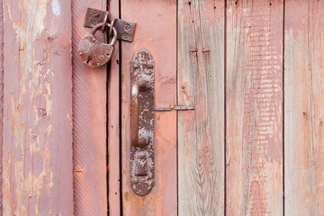 Old rusty metal padlock and door knob on a red wooden door. Closeup