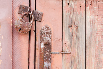 Old rusty metal padlock and door knob on a red wooden door. Closeup