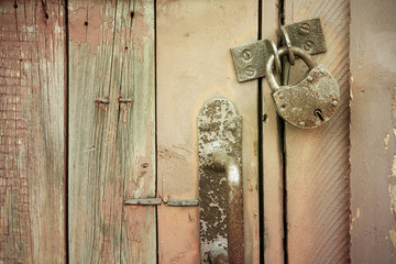 Old rusty metal padlock and door knob on a brown wooden door. Closeup, toned.