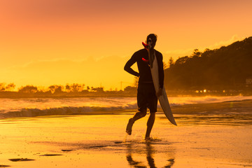 Surfer running on the beach at sunrise
