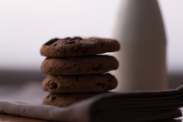 Stack of chocolate chips cookies and a bottle of milk on wooden background