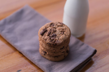 Stack of chocolate chips cookies and a bottle of milk on wooden background