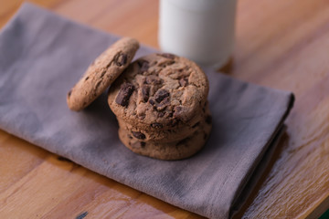 Stack of chocolate chips cookies and a bottle of milk on wooden background