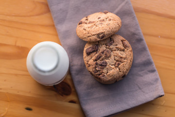 Stack of chocolate chips cookies and a bottle of milk on wooden background