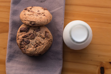 Stack of chocolate chips cookies and a bottle of milk on wooden background
