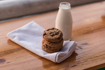 Stack of chocolate chips cookies and a bottle of milk on wooden background