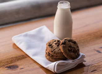 Stack of chocolate chips cookies and a bottle of milk on wooden background