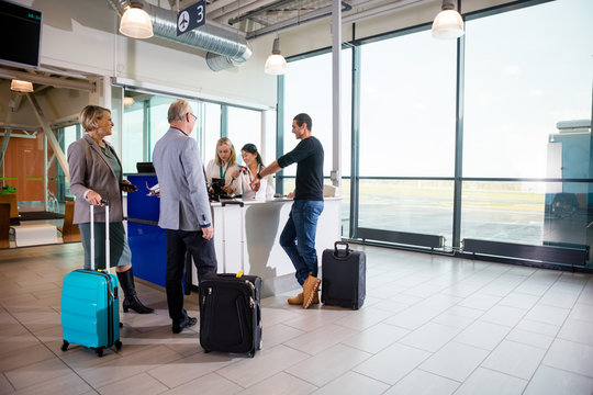 Passengers With Luggage Standing While Receptionists Working At 