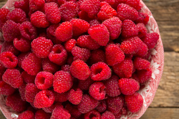 full bowl of raspberries on wooden surface